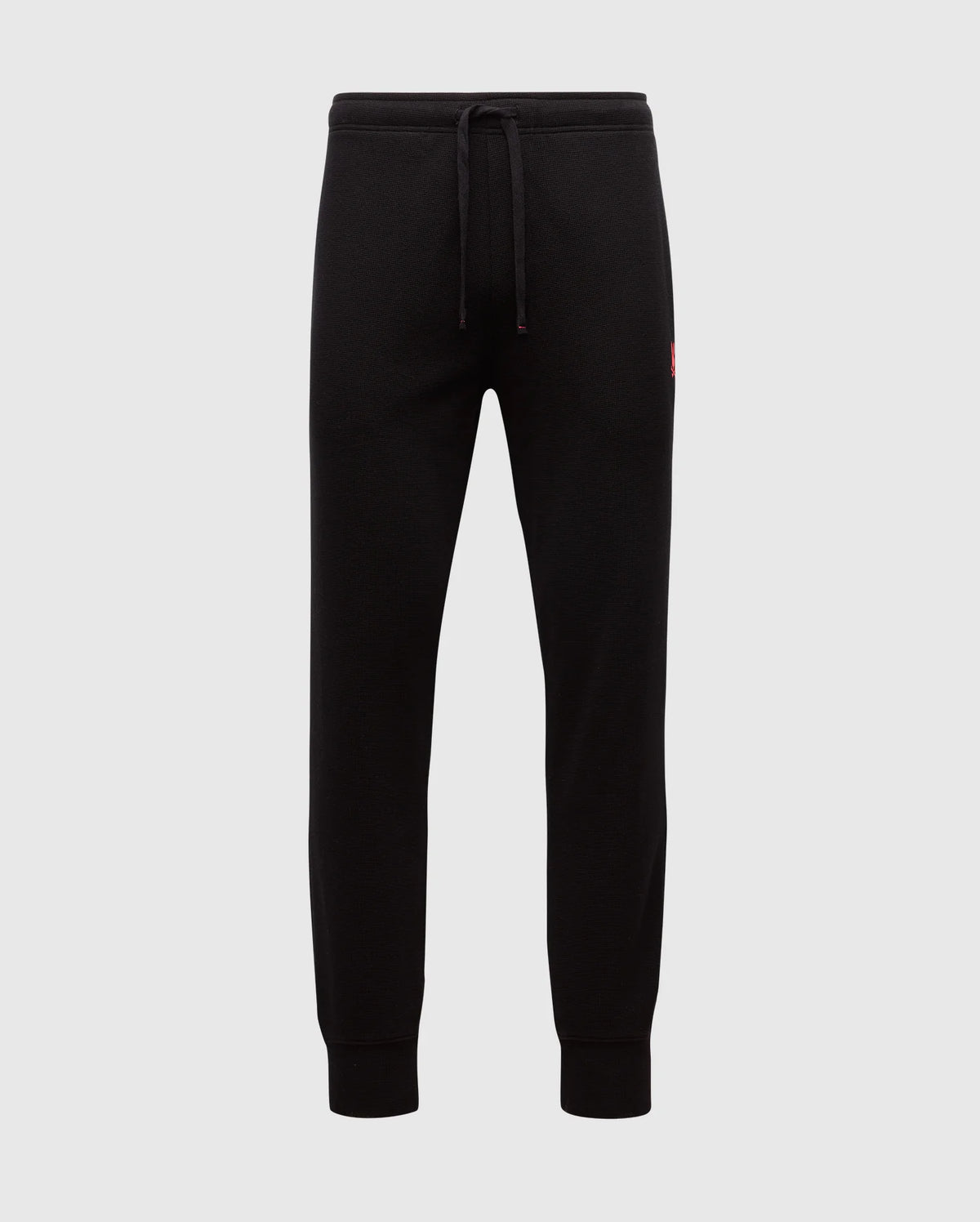 The MENS VAIL WAFFLE LOUNGE PANT - B6P673E200 by Psycho Bunny are black joggers made from a Pima Cotton Blend. They feature elastic cuffs and a drawstring waistband against a plain background, with a small red logo on the hip that underscores their comfort for lounging on relaxed days.