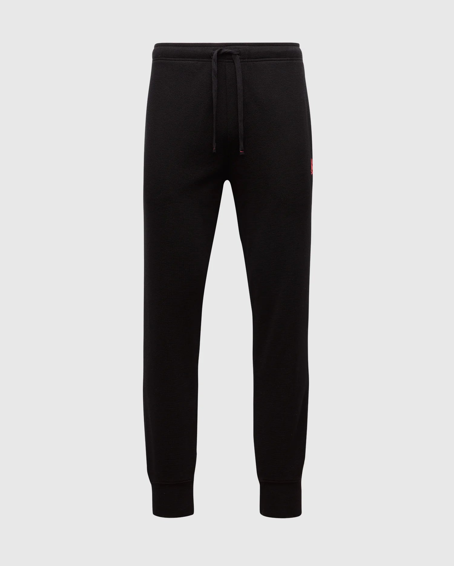 The MENS VAIL WAFFLE LOUNGE PANT - B6P673E200 by Psycho Bunny are black joggers made from a Pima Cotton Blend. They feature elastic cuffs and a drawstring waistband against a plain background, with a small red logo on the hip that underscores their comfort for lounging on relaxed days.