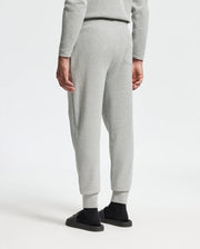 A person wearing a light gray sweatshirt and Psycho Bunny's MENS VAL WAFFLE LOUNGE PANT - B6P673E200 stands with their back to the camera. The outfit is paired with black shoes against a plain white background.