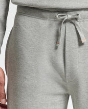 Close-up of a person's hand resting near the pocket of light gray Psycho Bunny MENS VAL WAFFLE LOUNGE PANT - B6P673E200. These lounge pants for men offer a drawstring waist and elastic band, ideal for achieving a laid-back look.