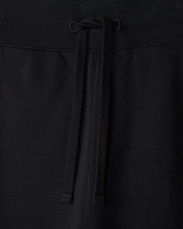 Close-up of the MENS LEVY ESSENTIAL FLEECE SWEATPANT - B6P721D200 by Psycho Bunny, showcasing black cotton sweatpants with an elastic waistband. The waistband features a matching black drawstring tied in a simple bow at the center. The texture of the fabric is visible, indicating comfort and durability, making them perfect for casual wear.
