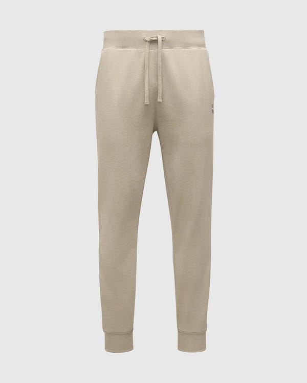The MENS LEVY ESSENTIAL FLEECE SWEATPANT - B6P721D200 by Psycho Bunny are beige, ultra-soft joggers for men. They feature an elastic waistband with a drawstring, cuffs at the ankles, and a small logo on the left thigh. Made from cozy cotton fabric, these sweatpants are soft and comfortable, making them ideal for casual wear.