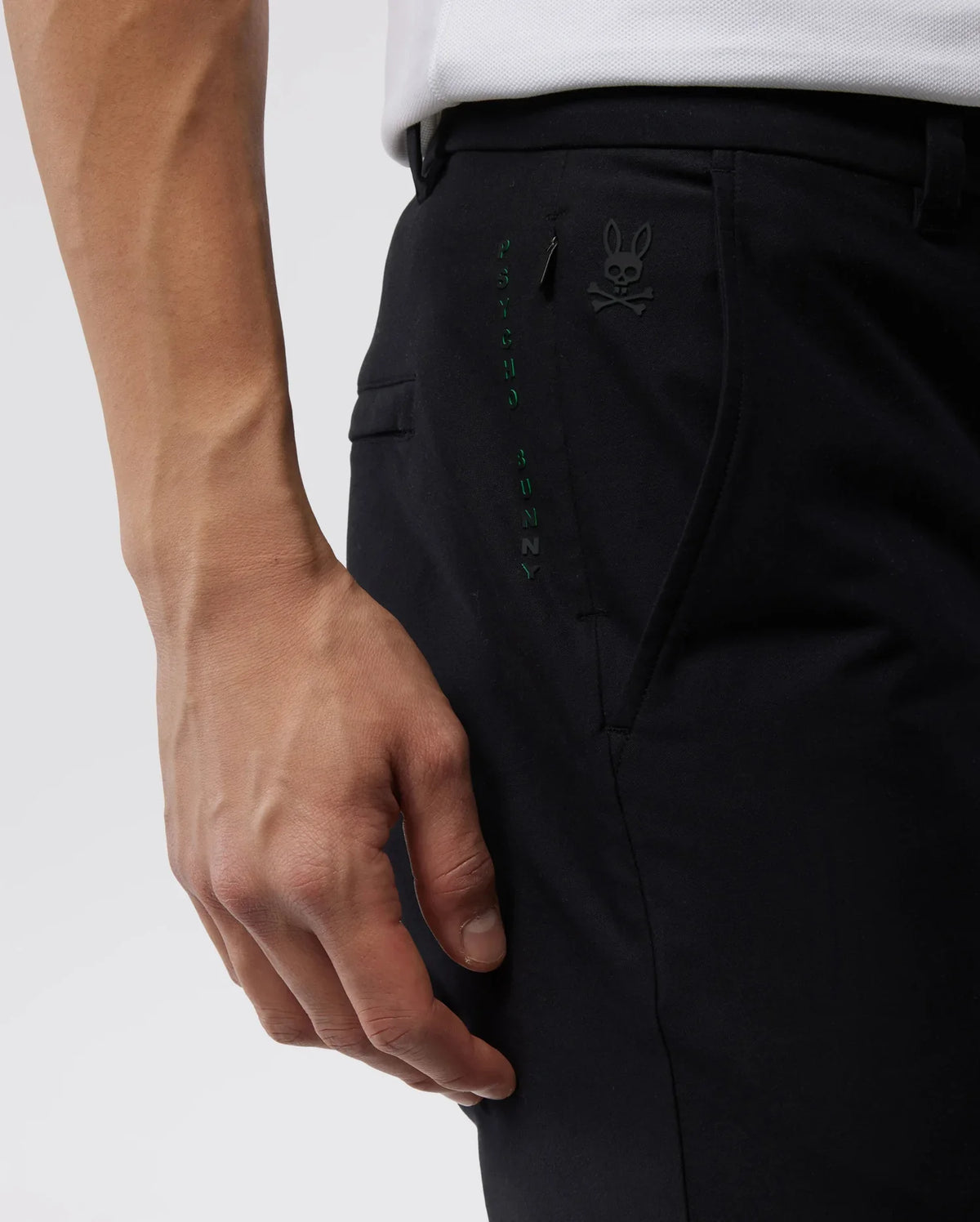 Close-up of a person's hand resting on the pocket of Psycho Bunny Men's Gable Regular Fit Sport Pants featuring a small HD Bunny print with a rabbit design.