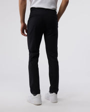 A man stands facing away from the camera, showing the back view of Psycho Bunny's Men's Gable regular fit sport pants paired with white sneakers on a light neutral background.