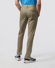 Rear view of a person wearing Psycho Bunny's MEN'S DELANCY CHINO PANTS - B6P784U1CO, a blue shirt, and white sneakers with black and blue accents against a plain light-colored background.
