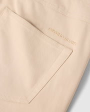 Close-up of the back pocket of a light beige, smooth and slightly glossy MENS 10K STEP PANT - B6P788D200 with the brand name "Psycho Bunny" embroidered in matching beige thread above the pocket. This sleek design features a comfortable four-way stretch for ease of movement.