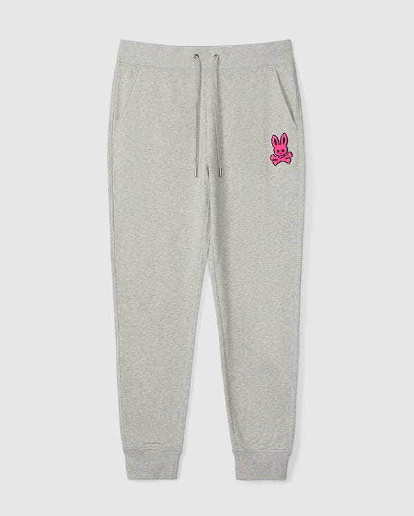 The SCOTT CHENILLE PATCH SWEATPANT by Psycho Bunny, product code B6P856D200, features a pink bunny and crossbones design on the left upper leg. It includes an elastic waistband with drawstrings and ankle cuffs.