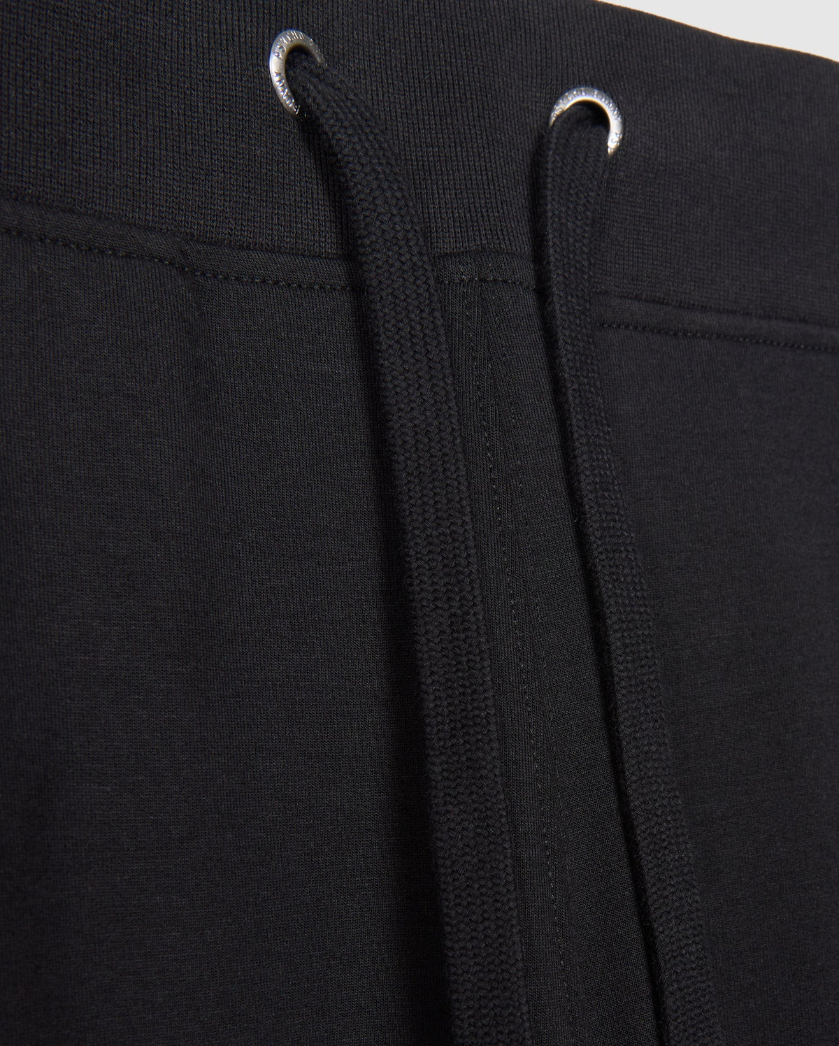 Close-up image of MENS WALTER LIGHTWEIGHT SWEATPANT - B6P860D200 by Psycho Bunny. The image focuses on the waistband area, showing the black drawstrings threaded through metal eyelets. The fabric appears to be knit or a similar material, ideal for casual wear with a breathable fit.