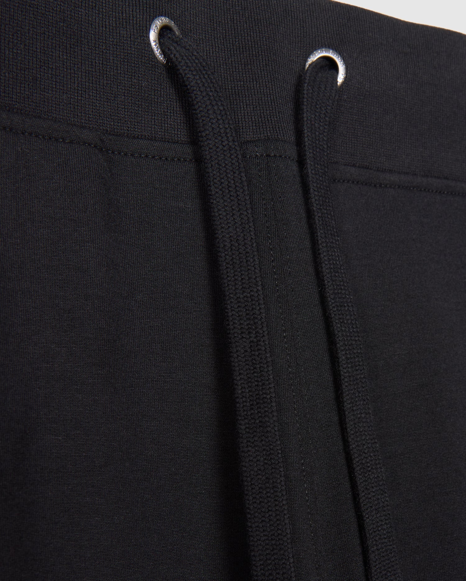 Close-up image of MENS WALTER LIGHTWEIGHT SWEATPANT - B6P860D200 by Psycho Bunny. The image focuses on the waistband area, showing the black drawstrings threaded through metal eyelets. The fabric appears to be knit or a similar material, ideal for casual wear with a breathable fit.