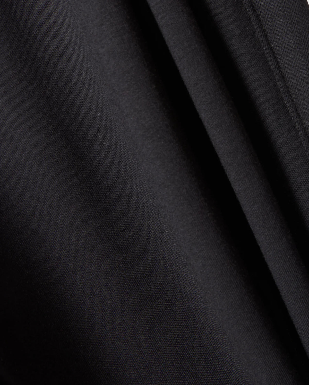 A close-up view of the black fabric material featured in Psycho Bunny's MENS WALTER LIGHTWEIGHT SWEATPANT - B6P860D200. The image captures smooth, uniform folds and a soft texture, with subtle shadows and highlights created by the draping. This indicates a lightweight and slightly glossy fabric that is perfect for casual wear or achieving a breathable fit in your favorite sweatpants.
