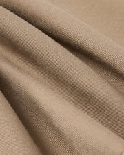 Close-up of the Psycho Bunny MENS HAYS TWILL PANT - B6P894D200, made from a soft beige cotton-blend twill with a textured surface featuring diagonal ridges. The four-way stretch material drapes in gentle folds, creating subtle shadows and highlights.