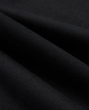 Close-up of Psycho Bunny's MENS HAYS TWILL PANT - B6P894D200, crafted from a black cotton-blend twill fabric with a diagonal ribbed texture. The material boasts four-way stretch, giving it a soft feel and a subtle sheen, with folds producing shadowy areas across the surface.