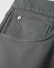 Close-up of the MENS HAYS TWILL PANT - B6P894D200 by Psycho Bunny, showcasing a pocket adorned with a small metallic button engraved with a minimalist face design. Situated on the pocket's upper corner, this dark gray cotton-blend twill garment exhibits 4-way stretch and features a textured, sturdy fabric.