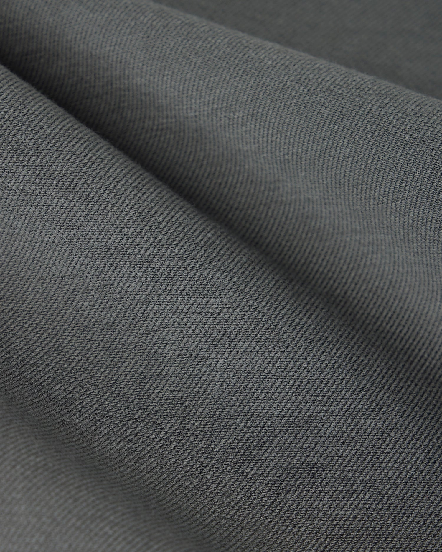 Close-up of the textured dark gray cotton-blend twill fabric from the Psycho Bunny MENS HAYS TWILL PANT - B6P894D200, featuring soft folds and a slightly ribbed pattern, highlighting its smooth surface and subtle color variations.