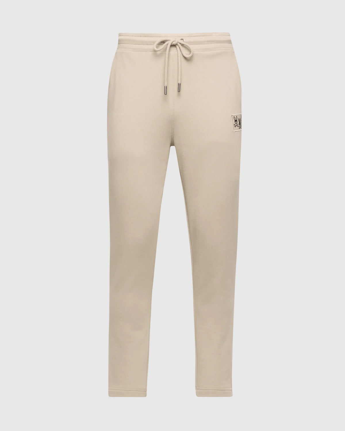 The Psycho Bunny Men's Monroe Twill Patch Fleece Sweatpant (B6P929D200) in beige, made from soft French terry, features a drawstring waistband and a small patch detail on the right hip. These sweatpants have a tapered fit against a plain white background.