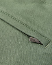 Close-up of a textured, green fabric featuring a sleek metallic zipper partially visible. The smooth fabric showcases intricate stitching details, reminiscent of the high-pile chenille logo patch found on the MENS PACIFIC CHENILLE JOGGER by Psycho Bunny.