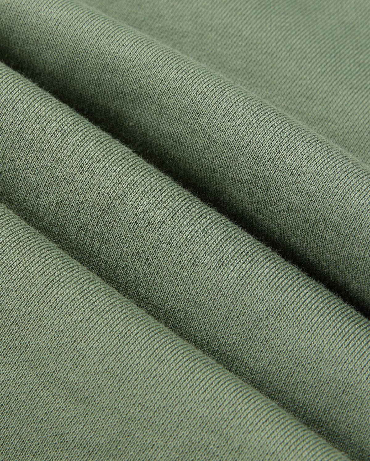 Close-up of green knitted fabric, highlighting its texture and soft appearance with visible weave patterns that evoke the cozy feel of Psycho Bunny's casual bottoms. The fabric is folded into gentle, evenly spaced ridges similar to the smooth drape of the MENS PACIFIC CHENILLE JOGGER - B6P972D200.