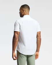 A person is facing away from the camera, wearing a Psycho Bunny MENS GABRIEL SHORT SLEEVE SHIRT (B6Q351F200) made from Pima cotton, paired with light green pants. The background is plain and light-colored.