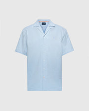 The Psycho Bunny MENS COBAR WOVEN SHIRT - B6Q522F200 is a light blue short-sleeve shirt with a collar and an embroidered logo on the chest. Made from cooling fabric, this simple, clean design is perfect beachwear for warm days.