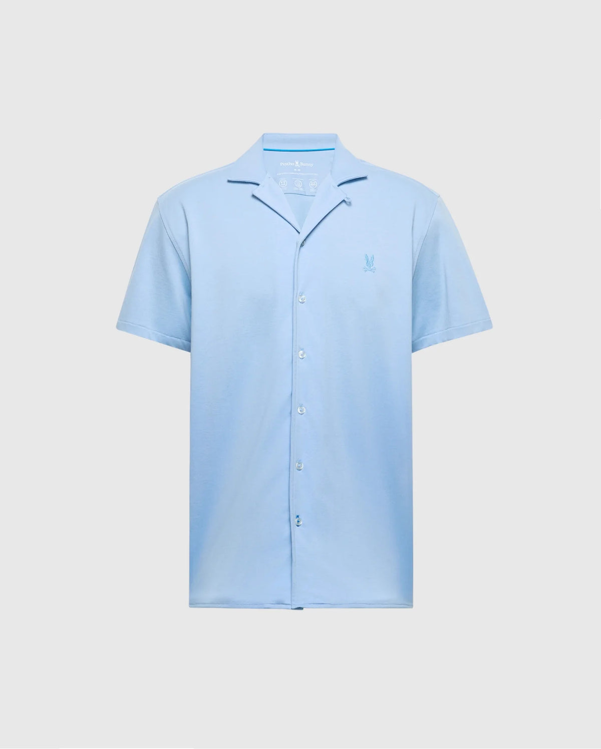 The Psycho Bunny MENS BRYAN CAMP COLLAR SHORT SLEEVE SHIRT in light blue features moisture-wicking performance fabric, a small embroidered chest logo, and a relaxed collar. It is displayed against a plain gray background. Model: B6Q581F200.