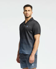 A man stands wearing the Psycho Bunny MENS BENDIGO TENCEL SHIRT in a black and blue ombre design with a camp collar, paired with matching shorts. Made from soft Tencel, his outfit complements his short curly hair and beard as he looks at the camera against a plain white background.