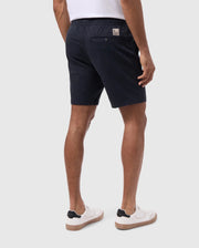 A person wearing navy blue Psycho Bunny York chino shorts and white sneakers photographed from the waist down against a plain white background.