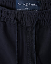 Close-up of navy blue sustainable MENS WILLIS STRETCH TENCEL shorts with a visible label displaying the brand "Psycho Bunny" and size "m-m" sewn into the waistband. The fabric has detailed