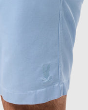 Close-up of a Psycho Bunny light blue shirt's short sleeve with a small, embroidered logo of a laurel wreath and a bird, against a white background.