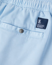 Close-up of a light blue Psycho Bunny Stretch Tencel short with a small embroidered "Psycho Bunny" logo patch and a silver button, displaying fine textile detail and neat stitching.
