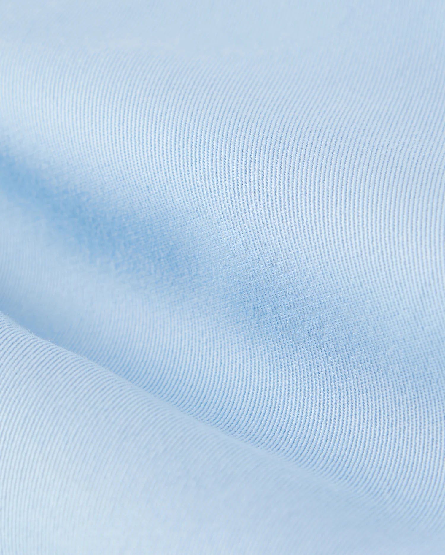 Close-up view of a light blue Psycho Bunny Mens Willis Stretch Tencel Short fabric texture showing fine knit details, slight variations in shade, and an embroidered logo.