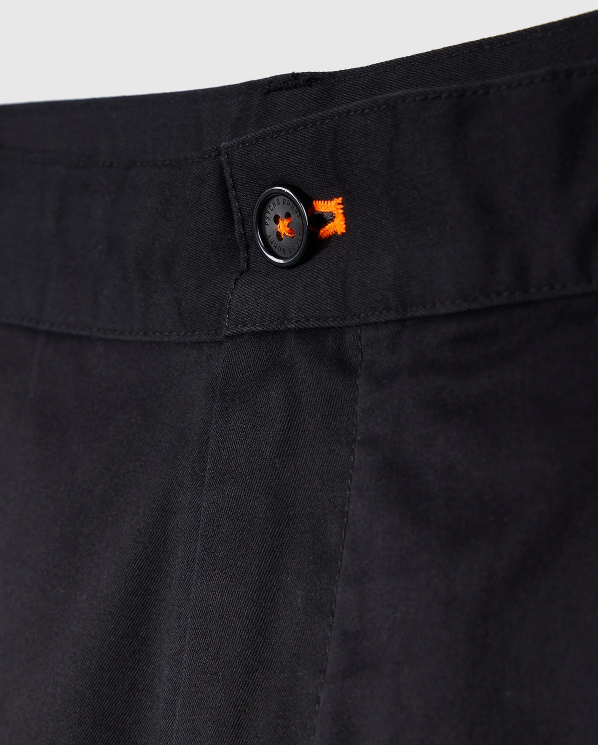 Close-up of a black trouser waistband featuring a button with an orange starburst design, emphasizing detail and texture in Psycho Bunny's Men's York Chino Shorts.