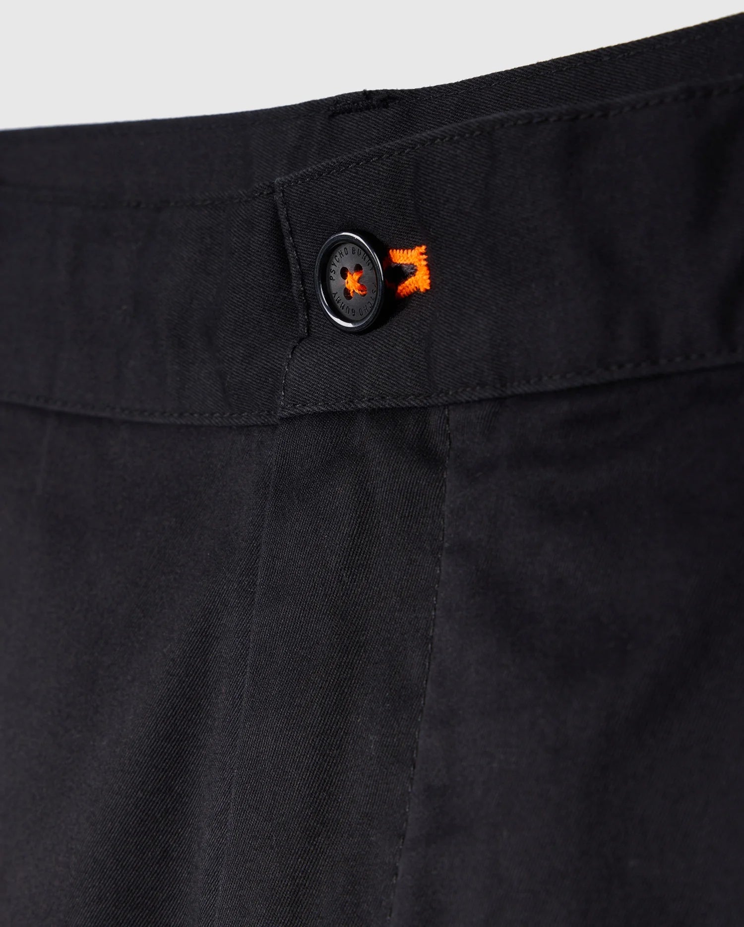 Close-up of a black trouser waistband featuring a button with an orange starburst design, emphasizing detail and texture in Psycho Bunny's Men's York Chino Shorts.