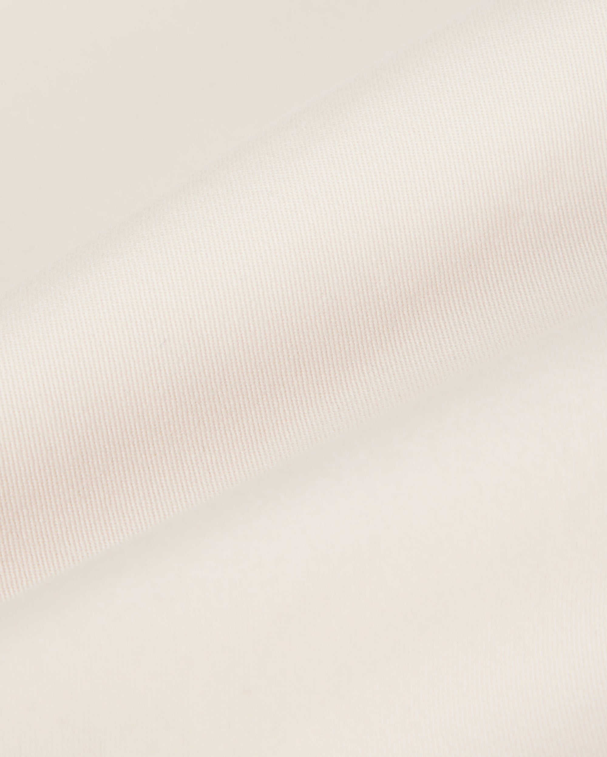 Close-up of a beige Psycho Bunny MEN'S YORK CHINO SHORT - B6R357B200 fabric with a smooth texture, showing a folded edge lying against a plain, soft background.