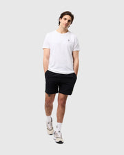 A person wearing a plain white t-shirt, Psycho Bunny MENS SONTERRA STRIPE SPORT SHORT - B6R464C200 made of quick-drying, breathable fabric, and white sneakers with socks stands casually with hands in pockets against a light-gray background. The person's head is slightly tilted to one side, and they have a relaxed expression.
