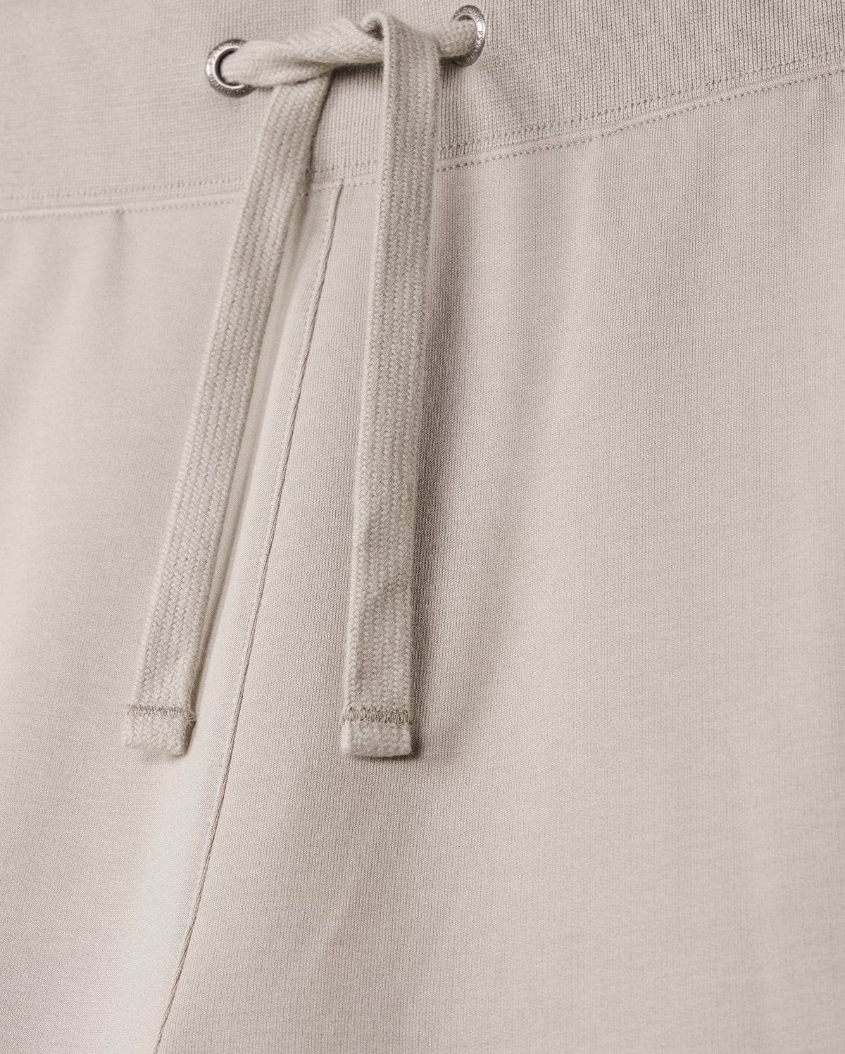 Close-up of the MENS WALTER LIGHTWEIGHT SWEATSHORT - B6R477D200 by Psycho Bunny, showcasing the waistband and tied drawstrings. The fabric, a high-quality cotton blend, appears soft and slightly textured, with metal grommets through which the drawstrings are threaded. The stitching along the regular fit waistband is visible.