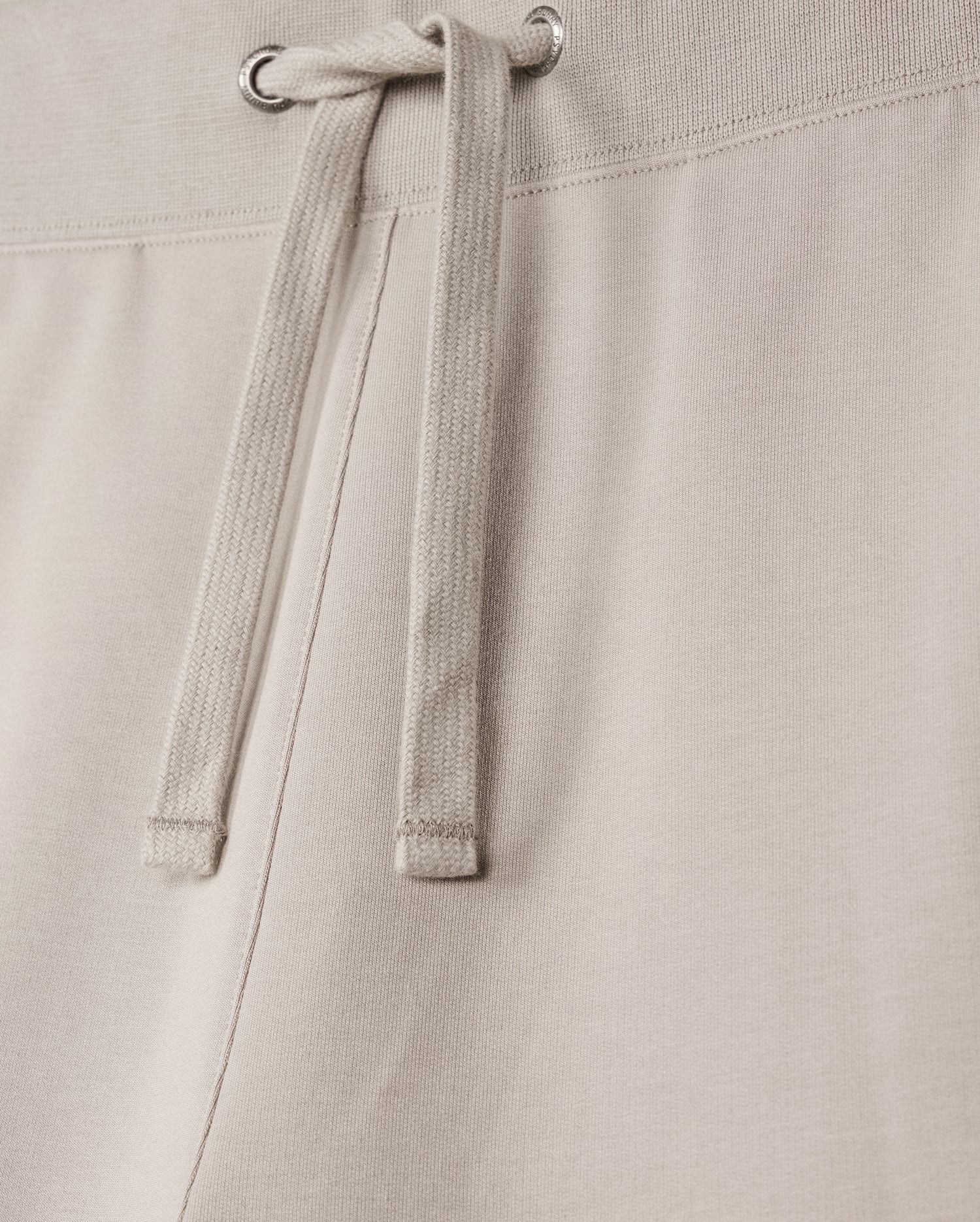 Close-up of the MENS WALTER LIGHTWEIGHT SWEATSHORT - B6R477D200 by Psycho Bunny, showcasing the waistband and tied drawstrings. The fabric, a high-quality cotton blend, appears soft and slightly textured, with metal grommets through which the drawstrings are threaded. The stitching along the regular fit waistband is visible.