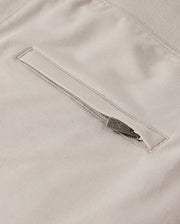 Close-up of the *MENS WALTER LIGHTWEIGHT SWEATSHORT - B6R477D200* by Psycho Bunny showcasing a light beige fabric with a horizontal zippered pocket. The zipper includes a metallic pull tab for easy access, and the surrounding fabric appears soft and smooth. This high-quality cotton blend ensures a uniform, finely woven texture in this lightweight sweatshort.