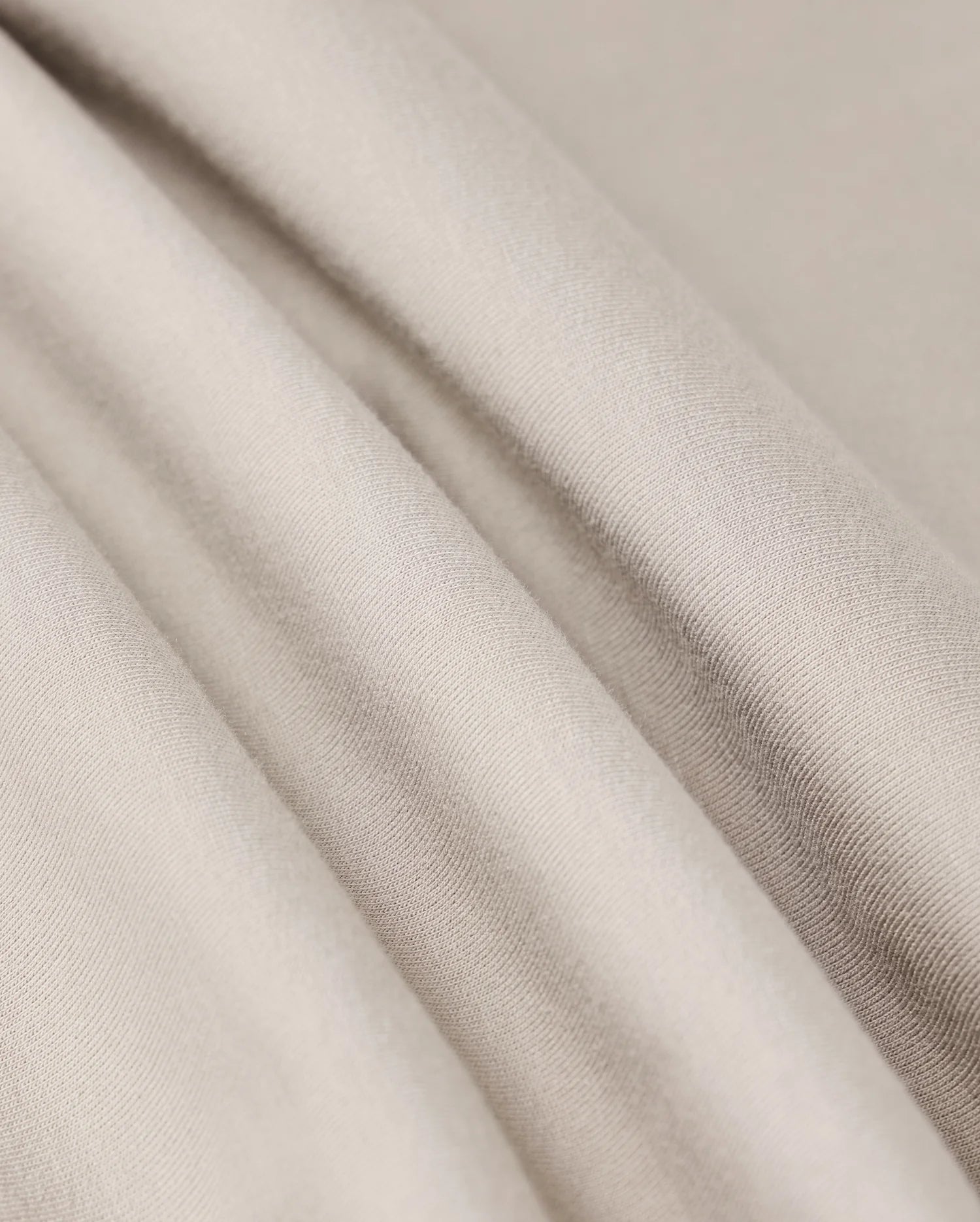Close-up image of the MENS WALTER LIGHTWEIGHT SWEATSHORT by Psycho Bunny, showcasing smooth, light beige fabric with soft folds. The high-quality cotton blend material appears lightweight and has a subtle sheen, highlighting the texture and gentle draping of the cloth.