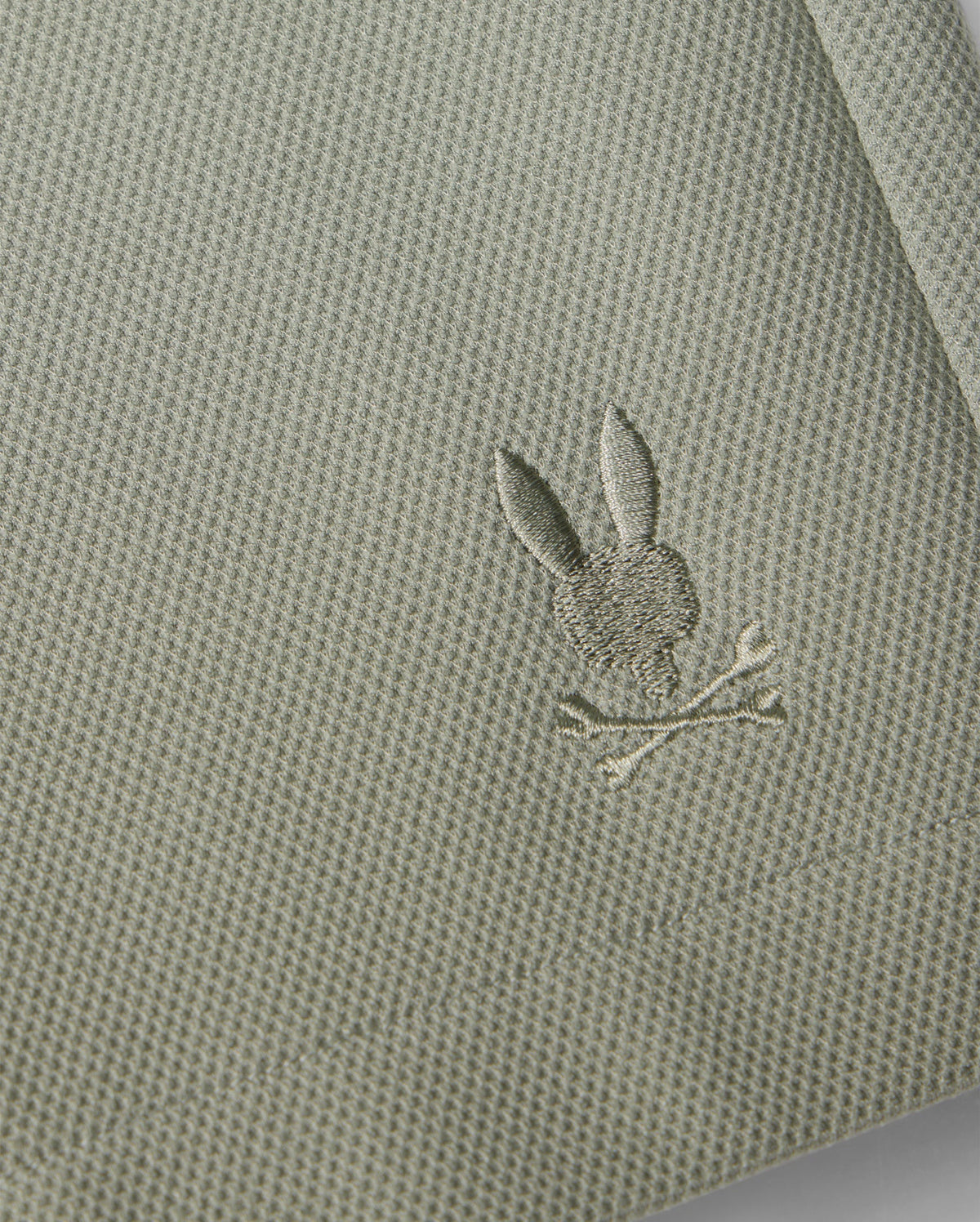 Close-up of a Psycho Bunny honeycomb fabric with a small, intricately embroidered silver rabbit holding a branch, stitched near the edge of the material.
