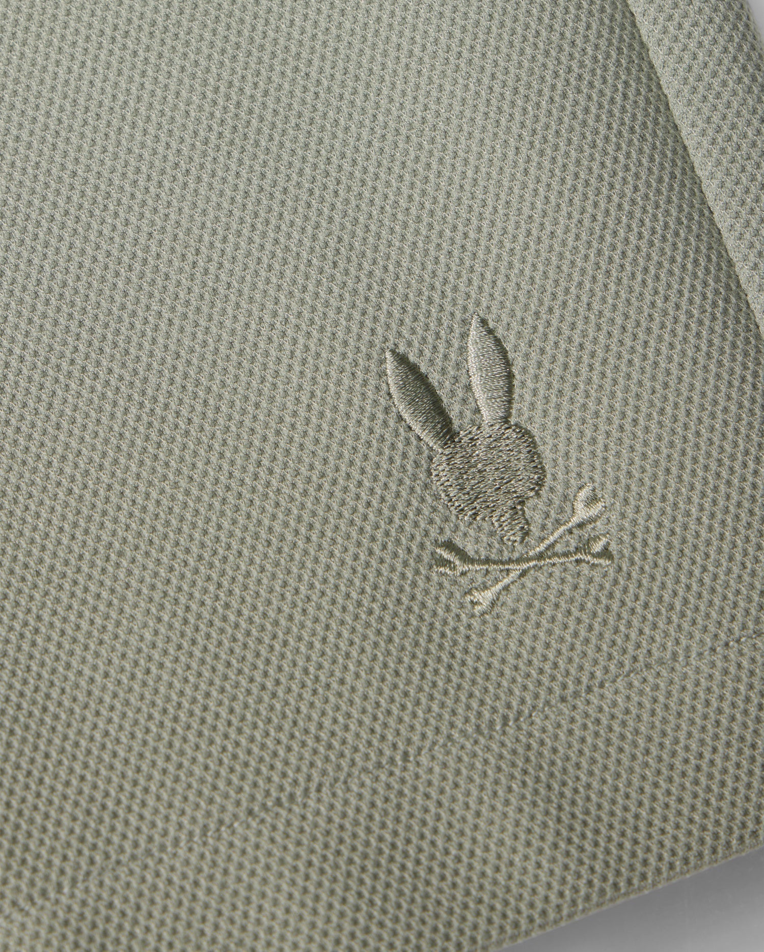 Close-up of a Psycho Bunny honeycomb fabric with a small, intricately embroidered silver rabbit holding a branch, stitched near the edge of the material.