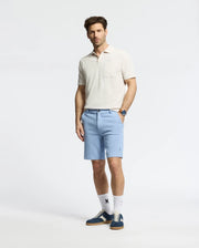 A dark-haired man stands against a plain background in light beige piqué with honeycomb texture, paired with light blue MENS SHIRO KNIT HONEYCOMB SHORT by Psycho Bunny. He's accessorized with a watch, white socks, and blue sneakers featuring a white leaf logo.