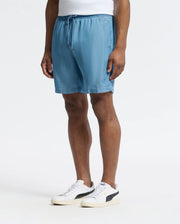 Wearing Psycho Bunny's MENS KERVIN LIGHTWEIGHT DENIM WOVEN SHORTS with an elasticized waist paired with white sneakers featuring black details, an individual is showcased from the waist down against a plain white background, embodying a casual and comfortable style.
