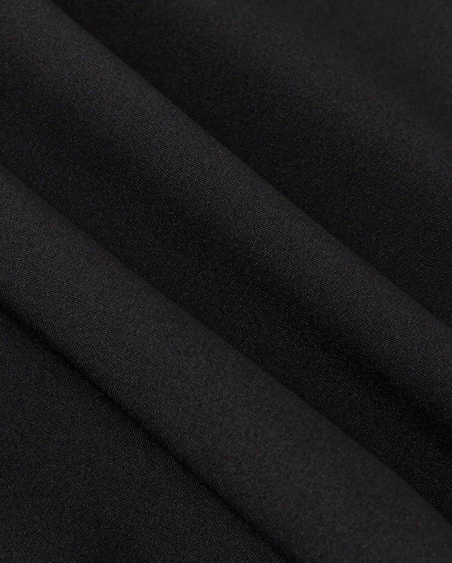 Close-up of smooth, black polyester fabric with visible folds, creating soft shadows and a subtle texture reminiscent of the MENS MANSFIELD SPORT SHORT - B6R807D200 by Psycho Bunny.