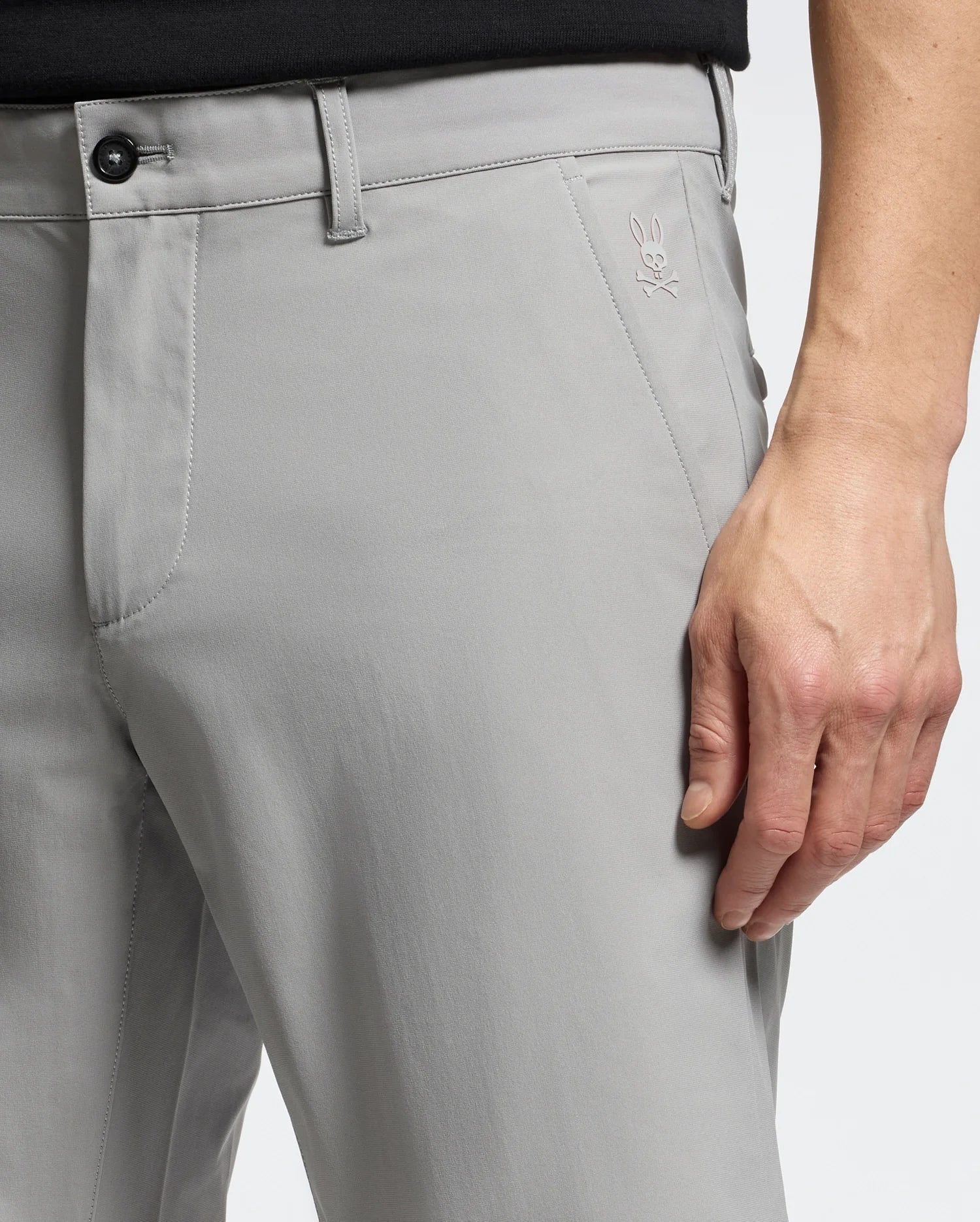 Close-up of a person wearing MENS 10K STEP SHORT - B6R969F200 by Psycho Bunny, with a subtle rabbit logo on light gray fabric. They pair it with a black top, right hand on their thigh, highlighting the shorts' fit and breathable texture for ultimate athletic comfort.