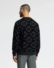 A man faces away from the camera, showcasing the MENS ROMEO LIGHTWEIGHT SWEATSHIRT - B6S129E200 by Psycho Bunny. This stylish black crew sweatshirt features a pattern of bunnies and "PSYCHO BUNNY" text in gray and is paired with gray pants, all set against a plain background.