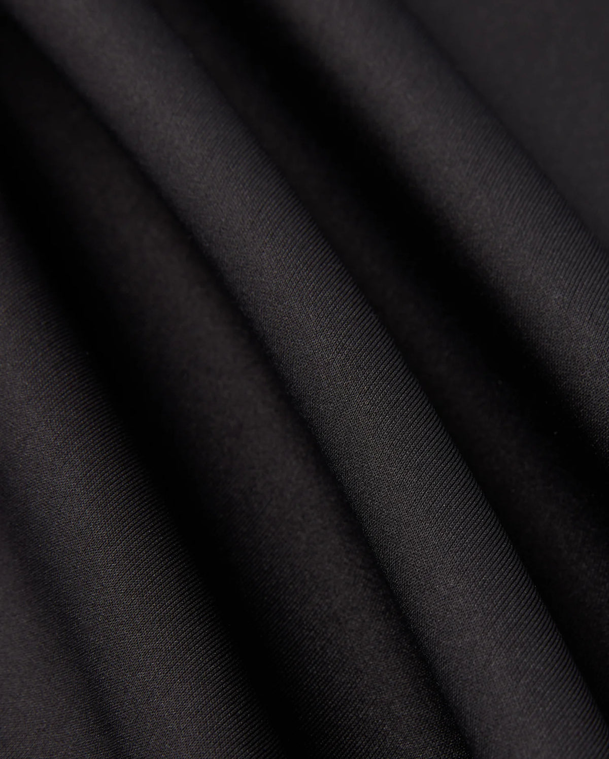 Close-up of the Psycho Bunny MENS LAURIER 1/4 ZIP HOODIE - B6S149D200 in black, crafted from cotton jersey fabric with soft, flowing folds and a smooth texture. The hoodie exudes an elegant, slightly reflective quality, embodying an athleisure aesthetic as it captures light along its gentle curves.