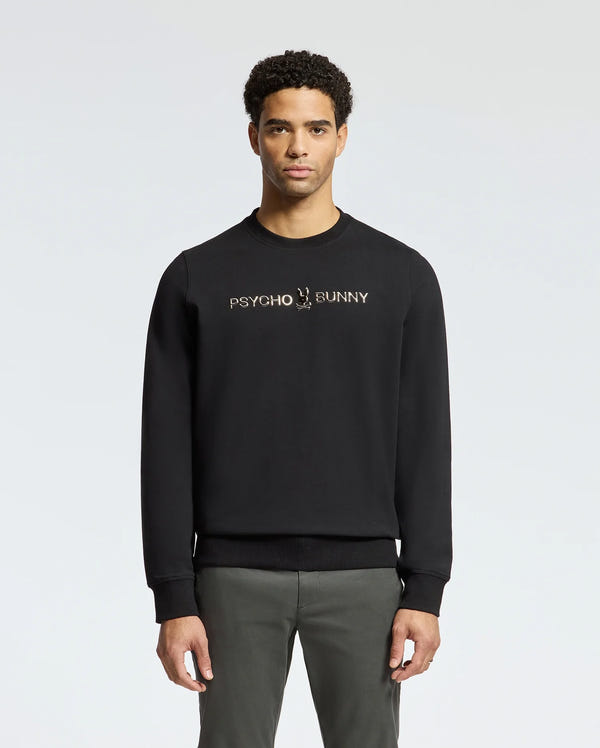 A man stands facing forward wearing the stylish MENS LAVETA FRENCH TERRY SWEATSHIRT - B6S159E200 by Psycho Bunny, featuring "Psycho Bunny" in white on the chest. This comfortable black cotton crew sweatshirt pops against a simple, light-colored background.