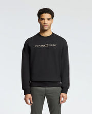 A man stands facing forward wearing the stylish MENS LAVETA FRENCH TERRY SWEATSHIRT - B6S159E200 by Psycho Bunny, featuring "Psycho Bunny" in white on the chest. This comfortable black cotton crew sweatshirt pops against a simple, light-colored background.