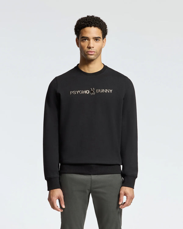 A man stands facing forward wearing the stylish MENS LAVETA FRENCH TERRY SWEATSHIRT - B6S159E200 by Psycho Bunny, featuring "Psycho Bunny" in white on the chest. This comfortable black cotton crew sweatshirt pops against a simple, light-colored background.