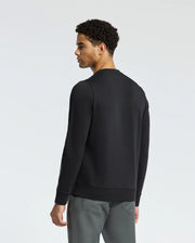A man with short curly hair is wearing the black, lightweight MENS OAK CITY CREW NECK - B6S274E200 by Psycho Bunny and gray pants, standing against a plain white background. The premium quality of his attire is evident as he faces slightly away from the camera.